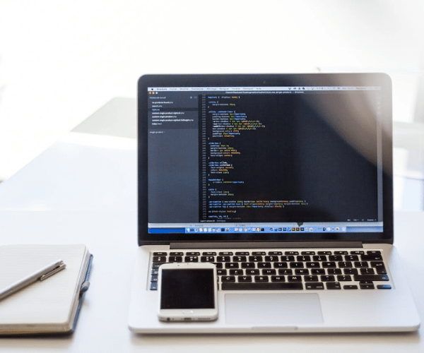 Laptop with coding screen and smartphone on desk, showcasing an App Development Company in Kochi.